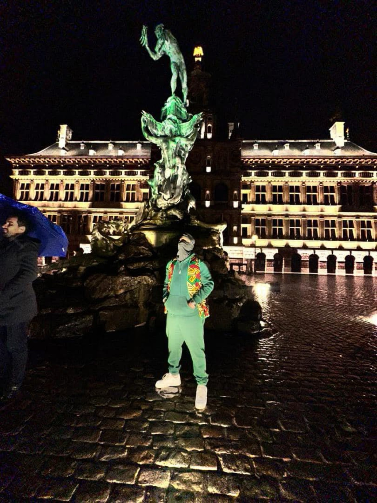 Le Mélangeur masqué, en survêtement vert, devant la fontaine Brabo à Anvers, de nuit
